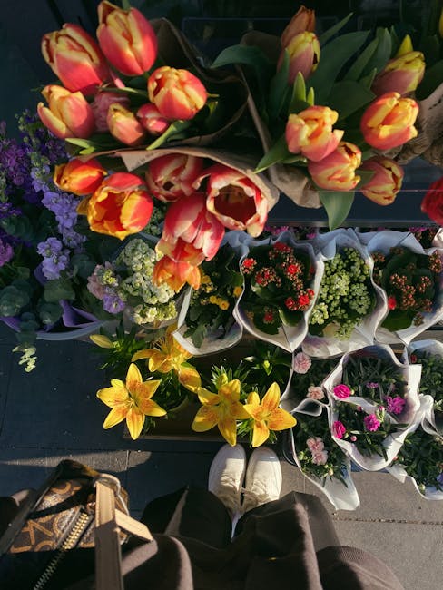 An overhead view of a flower display at a florist shop, featuring a variety of fresh floral arrangements and bouquets. Prominently, there is a large bouquet of tulips with orange and yellow petals, ar